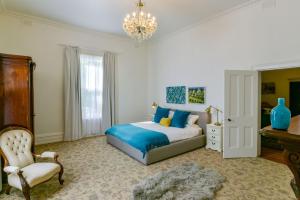 a bedroom with a bed and a chair and a chandelier at Elm Tree Lodge Beechworth in Beechworth