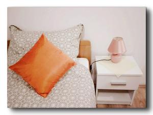 ein Bett mit einem orangefarbenen Kissen und ein Nachttisch mit einer Lampe in der Unterkunft Studio Leonidas Vis in Vis