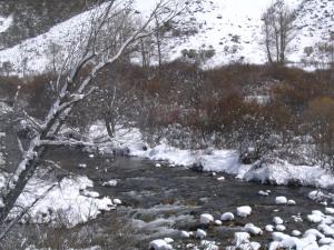 a stream with snow on the ground next to a snow covered slope at Hostal Asador La Montaña in Triollo