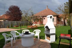 a backyard with a fireplace and white chairs and a table at Liliom Apartman in Gyula