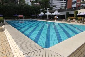ein großer blauer Pool mit Stühlen und Sonnenschirmen in der Unterkunft Fiesta Bahia Hotel in Salvador