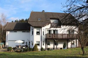 Cette grande maison blanche dispose d'un balcon. dans l'établissement Ferienwohnung am Eifelsteig Vulkaneifel-Auszeit, à Trittscheid
