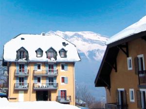 a building with a snow covered roof with a mountain at Lagrange Vacances Les Arolles in Saint-Gervais-les-Bains