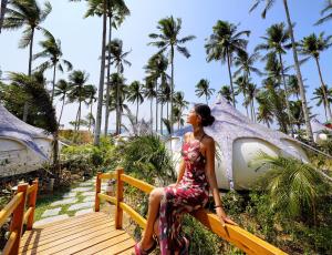 a woman in a dress sitting on a wooden bridge in front of palm trees at Nacpan Beach Glamping Managed by H Hospitality Group in El Nido
