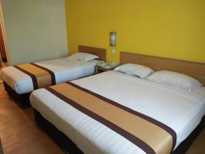 two beds in a hotel room with yellow walls at Tang Dynasty Lodge Tuaran in Tuaran