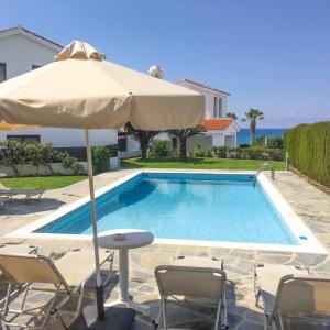 a swimming pool with an umbrella and chairs and a table with an umbrella at Platzia Beach Villas in Paphos