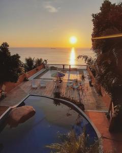 um pôr-do-sol sobre uma piscina com vista para o oceano em Memorial Ilhabela residencial em Ilhabela