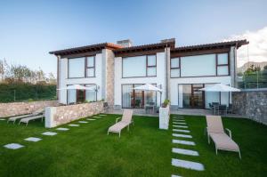 a house with a lawn with chairs and umbrellas at Bufones de Pria Apartamentos Rurales in Garaña