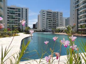 a swimming pool with some pink flowers in front of some buildings at Apartamento 2 quartos Living Park Sul in Brasília