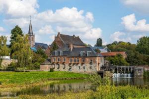 an old building next to a river with a church at Chalet à fleur de rêve in Maroilles