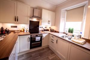 a kitchen with white cabinets and a sink and a stove at Butler's Apartment. Flat 5, Dalmore House, Helensburgh, Scotland G84 8JP in Helensburgh