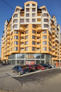un grand bâtiment jaune avec des voitures garées dans un parking dans l'établissement Luxury Apartament 2, à Trouskavets