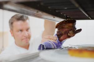 a man is holding a piece of meat in an oven at Hotel Reussischer Hof in Schmölln