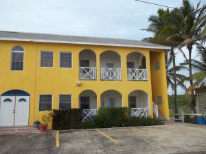 a yellow building with white doors and a palm tree at Ocean Ridge at Long Beach in Christ Church
