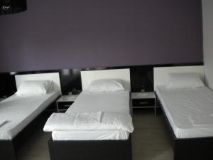 three beds in a room with white sheets and pillows at Hotel Leder in Kočani