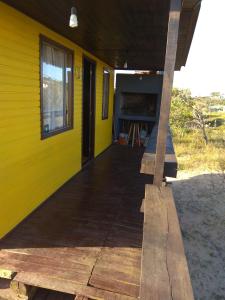 a yellow house with a wooden porch with a window at Fama in Punta Del Diablo