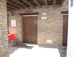 una puerta de madera en una pared de ladrillo con una silla roja en Apartamentos El Mirador en Bérchules