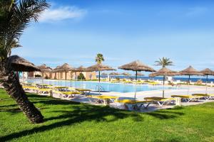 a swimming pool with chairs and umbrellas and the ocean at AQI Skanes Resort in Monastir