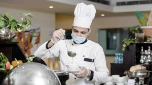 Um chef está a mexer uma tigela com uma colher. em Onizah Hotel em Unayzah