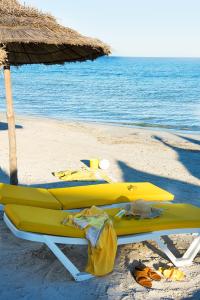 a yellow lounge chair on a beach with an umbrella at AQI Skanes Resort in Monastir