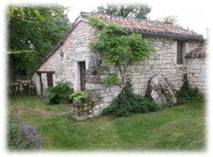 une vieille maison en pierre avec un arbre en face de celle-ci dans l'établissement Ferme de Laspeyrières, à Montcuq
