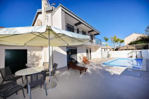 eine Terrasse mit einem Tisch, einem Sonnenschirm und einem Pool in der Unterkunft Villa Lily ZadarVillas in Privlaka