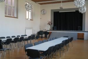 une salle avec des tables, des chaises et une scène dans l'établissement Emmaus Hostel, à Haslev