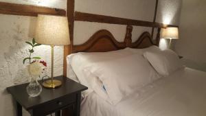 Una cama con sábanas blancas y un jarrón de flores en una mesita de noche en Hotel Labranza en San Martín de Valdeiglesias
