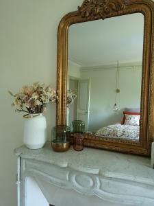 a mirror on a table with a vase and flowers at Le Clos des Fées in Asnières-sur-Oise