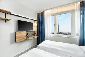 a bedroom with two beds and a tv and a window at H2 Hotel München Olympiapark in Munich