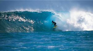 un homme faisant une vague sur une planche de surf dans l'océan dans l'établissement Ocean Breeze Bungalow, à Tevaitoa