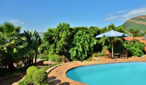 a swimming pool with an umbrella and a table and chairs at Stirling Manor Boutique Guest House in Hartbeespoort