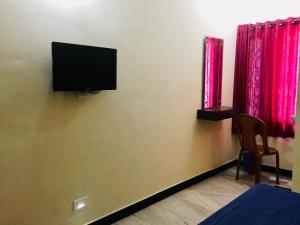 a room with a tv on a wall with red curtains at Hotel John in Kanyakumari
