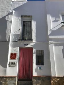 Edificio blanco con puerta roja y balcón en Casa las tres Conchas (2) en Yunquera