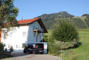 una furgoneta negra estacionada frente a una casa blanca en Ferienwohnung Gipfelstürmer, en Bolsterlang