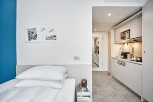 a bedroom with a white bed and a kitchen at H.ome Serviced Apartments München in Munich