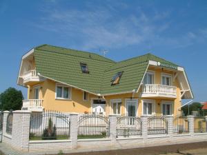 a yellow house with a green roof on top of a fence at Margaréta Apartmanház in Hajdúszoboszló