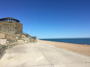 an empty sidewalk next to the ocean with a lighthouse at STAPLEHURST COTTAGE in Sandgate