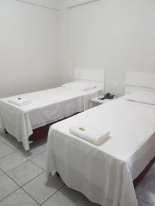 um quarto com três camas com lençóis brancos em Leal Classic Hotel em Itabuna