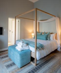 a bedroom with a canopy bed and a blue ottoman at Bentley's Guesthouse in Bloubergstrand +36 photos