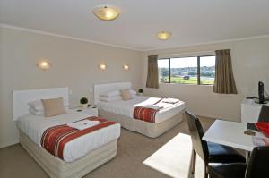a hotel room with two beds and a table and a desk at Airport Harbour Motel in Auckland