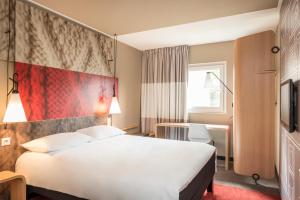 um quarto de hotel com uma cama branca e uma parede vermelha em ibis Gonesse em Gonesse