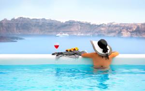 a person in the water with a table and a glass of wine at CAPE 9 Villas & Suites in Akrotiri