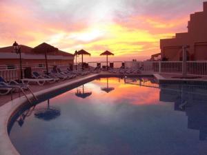een zwembad met stoelen en parasols bij zonsondergang bij Charming Sunset View Apt Heater Pool Costa Adeje in Adeje