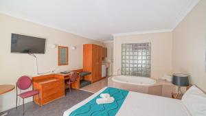 Country 2 Coast Motor Inn Coffs Harbour في كوفس هاربور: غرفة نوم مع سرير ومكتب وحوض استحمام
