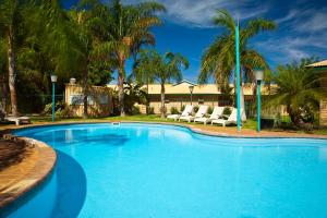 a swimming pool with chairs and palm trees at Potshot Hotel Resort in Exmouth
