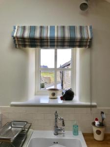 ventana de cocina con cortina a rayas sobre un fregadero en The Hay Loft Southlands Farm en Gunnerton