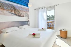 a white bedroom with a large white bed with towels at Logis Les Vagues in Biscarrosse-Plage