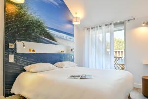 a bedroom with a white bed with a painting on the wall at Logis Les Vagues in Biscarrosse-Plage