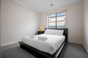 a white bedroom with a large bed with a window at Holiday Rose in Point Cook
